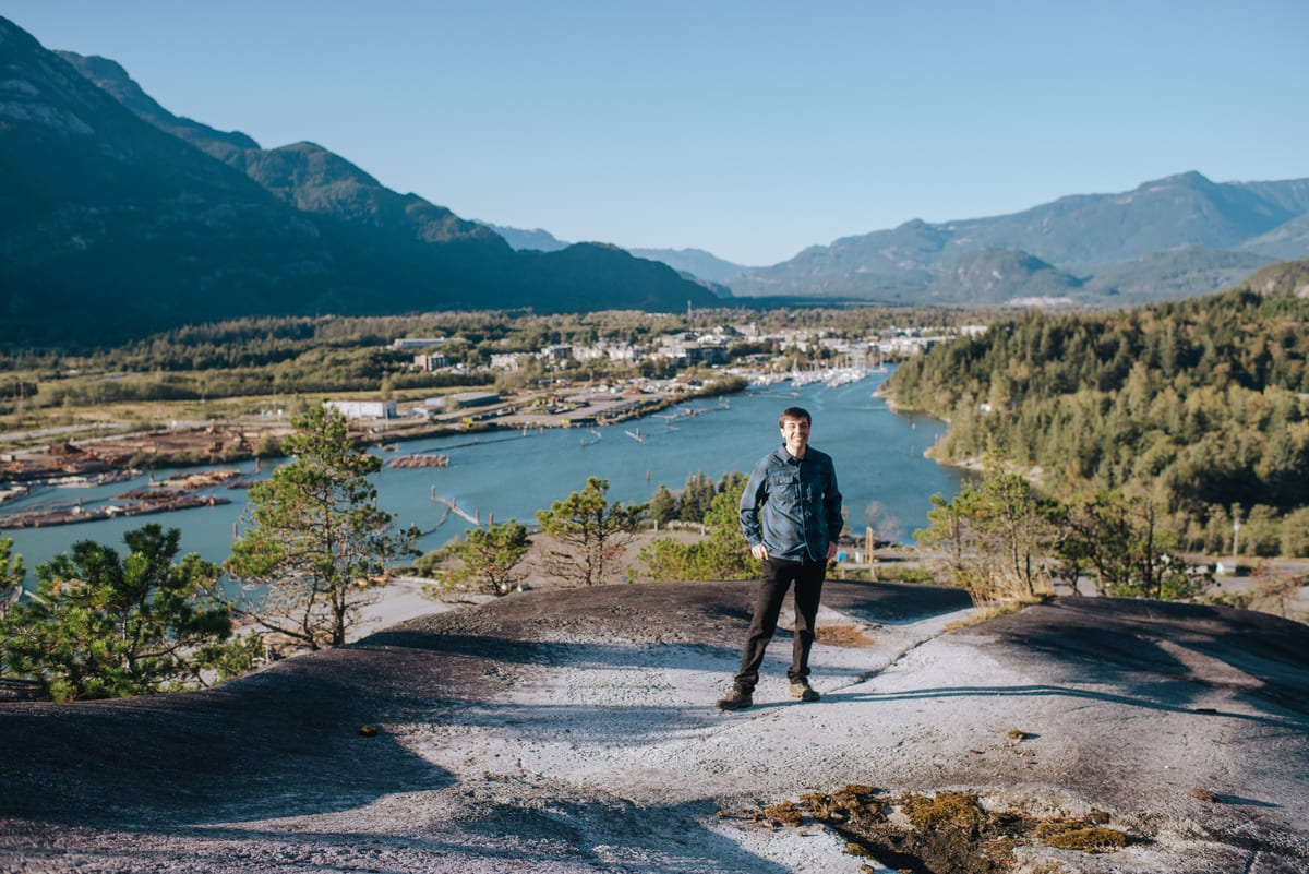 Chris Pettingill standing on the granite bluffs above Squamish, with the estuary, town and mountains behind him